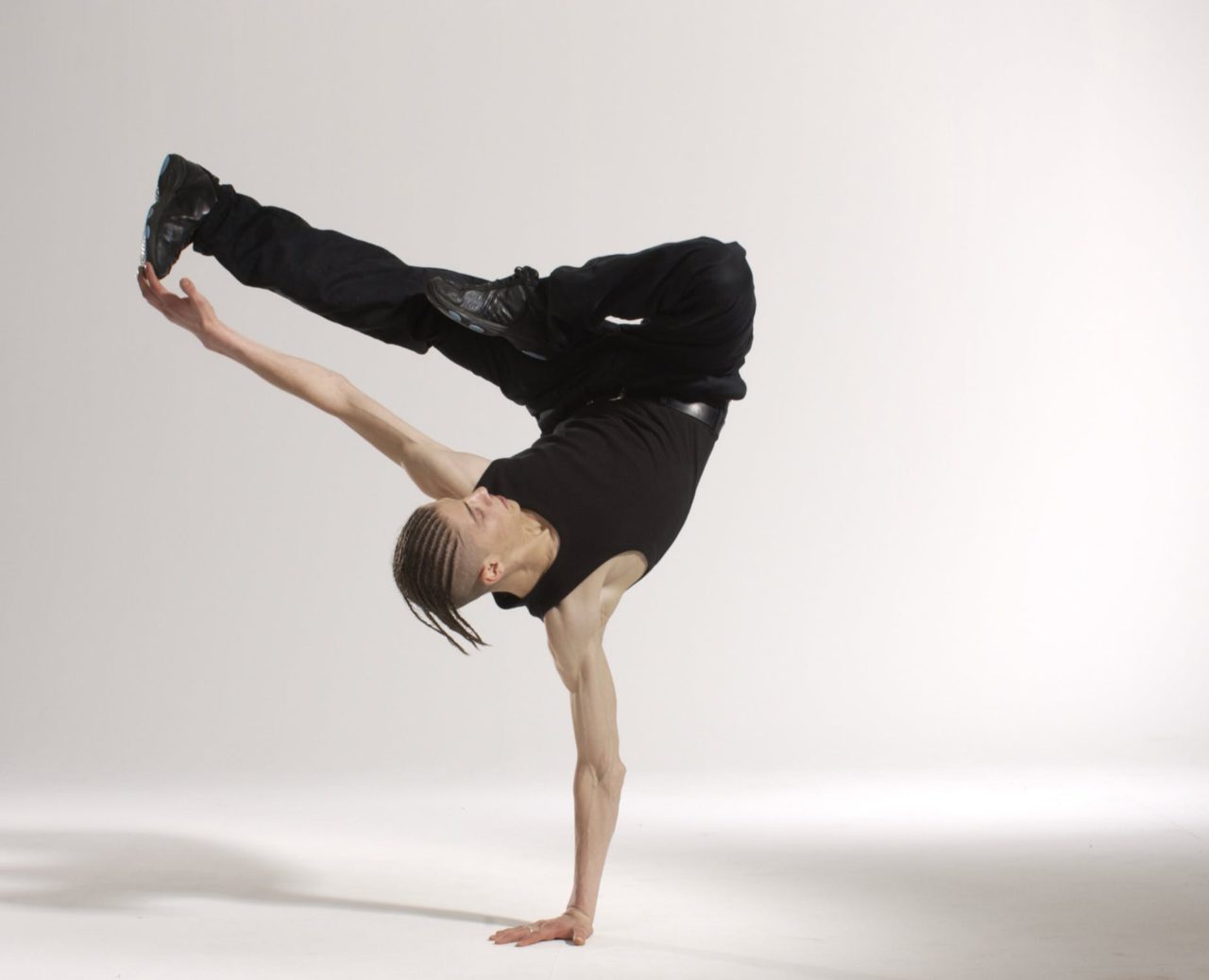 man wearing all black break dancing with a white background