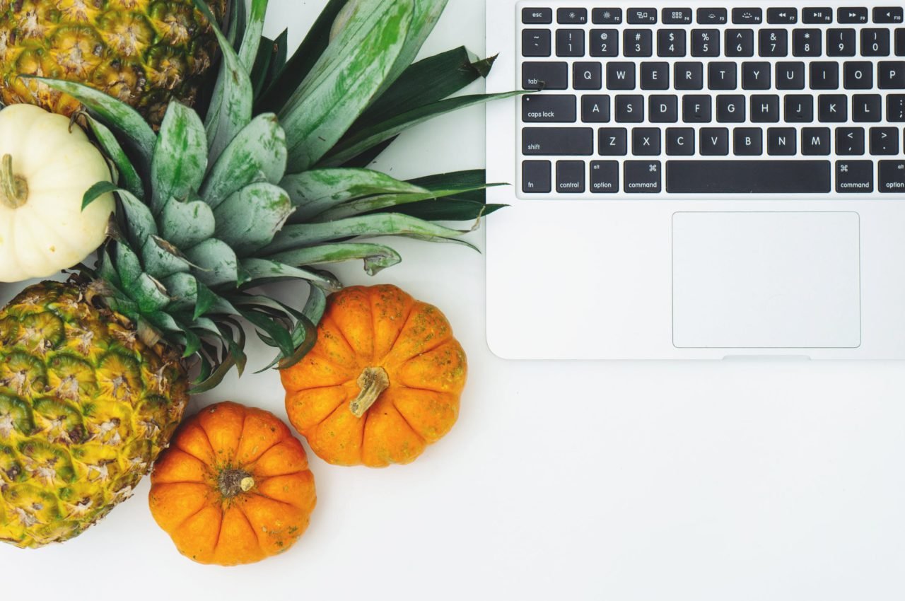 laptop next to a pineapple and some small pumpkins